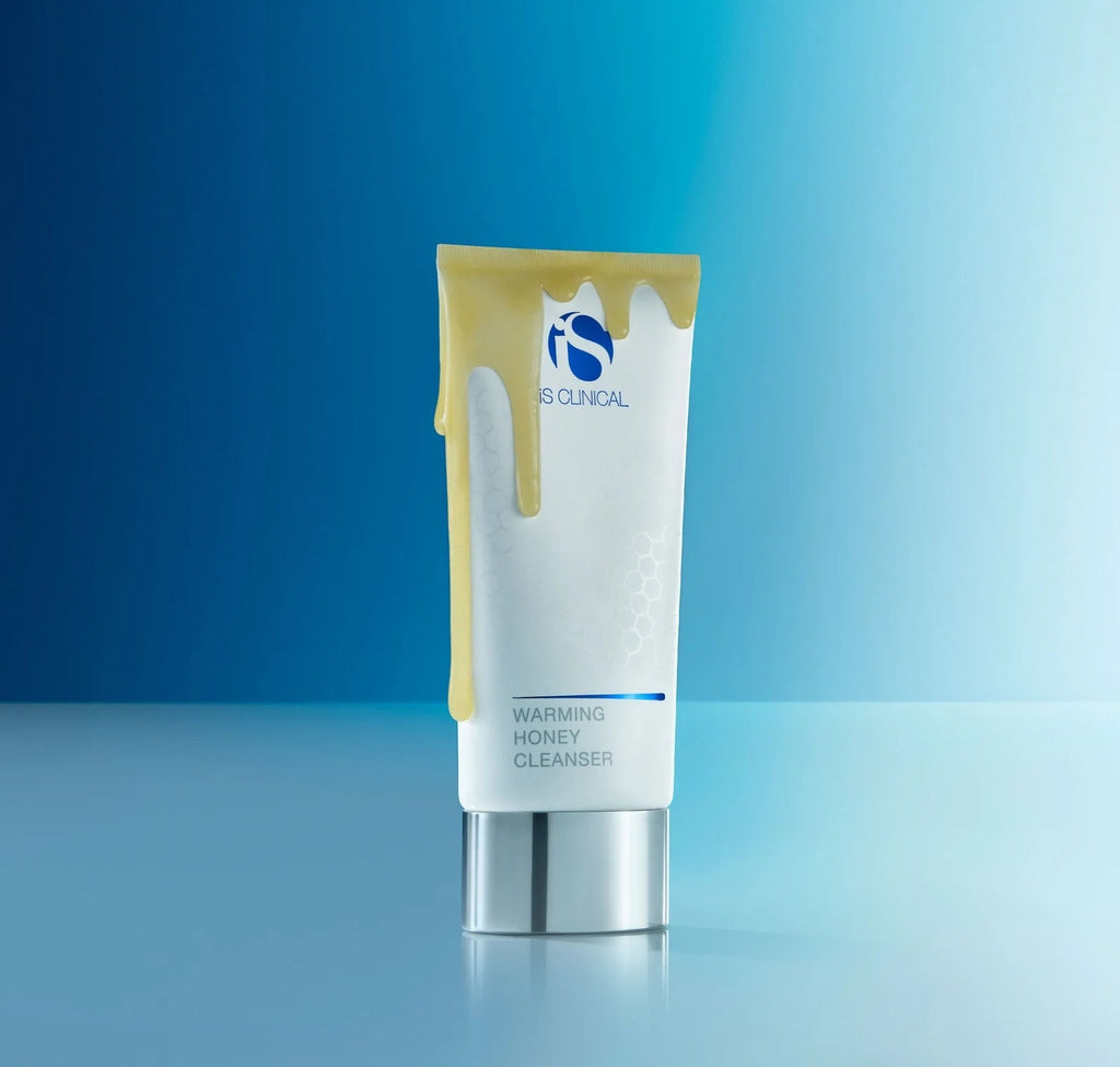 Tube of IS Clinical Warming Honey Cleanser on a gradient blue background